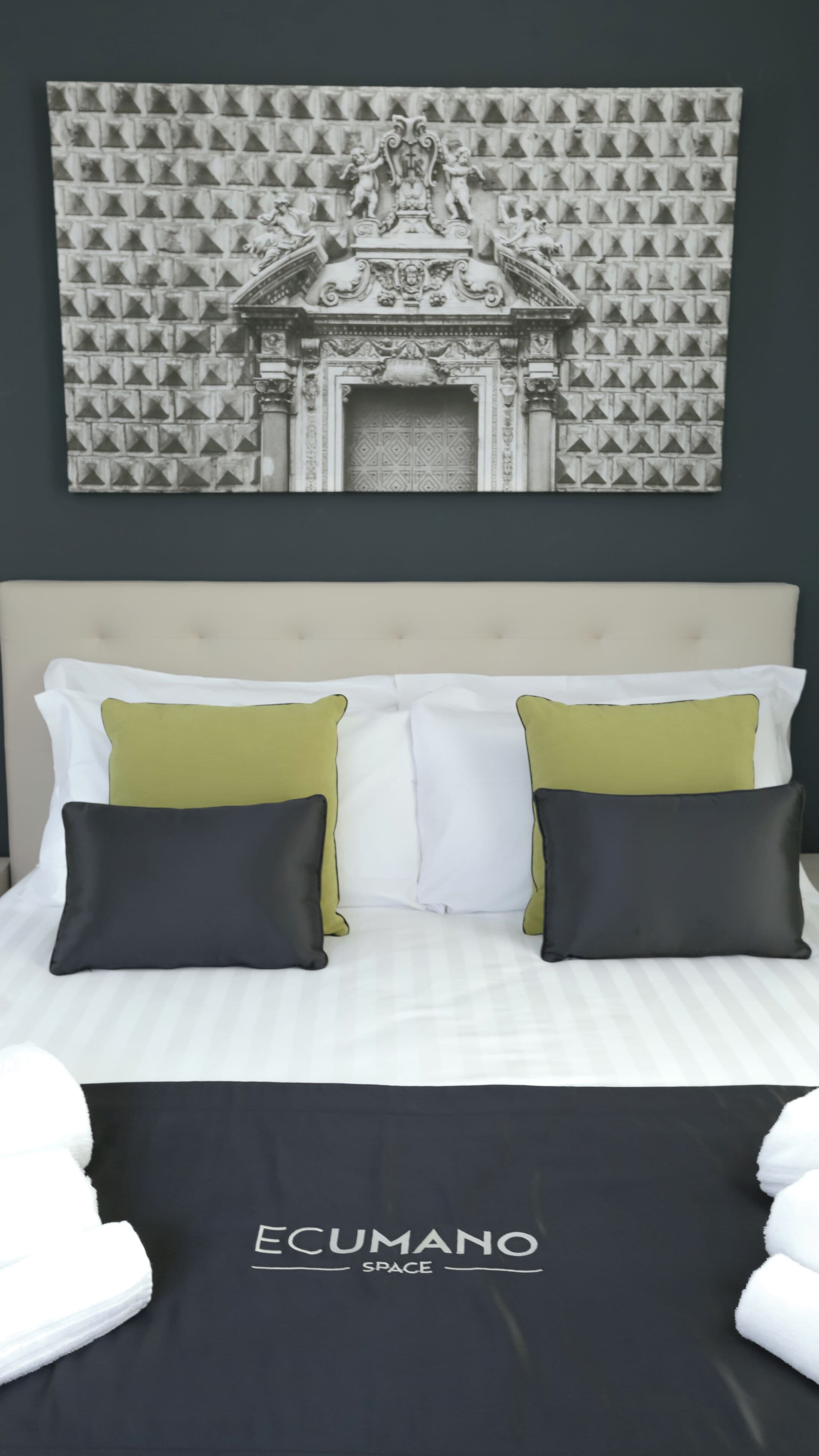 Una cama con almohadas blancas y verdes, un cabecero y una pared con una obra de arte estampada arriba.