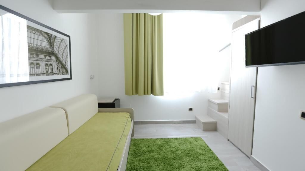Una habitación moderna con un sofá blanco, un tapete verde, una ventana con cortinas, un televisor de pantalla plana y una escalera que lleva a un nivel superior.