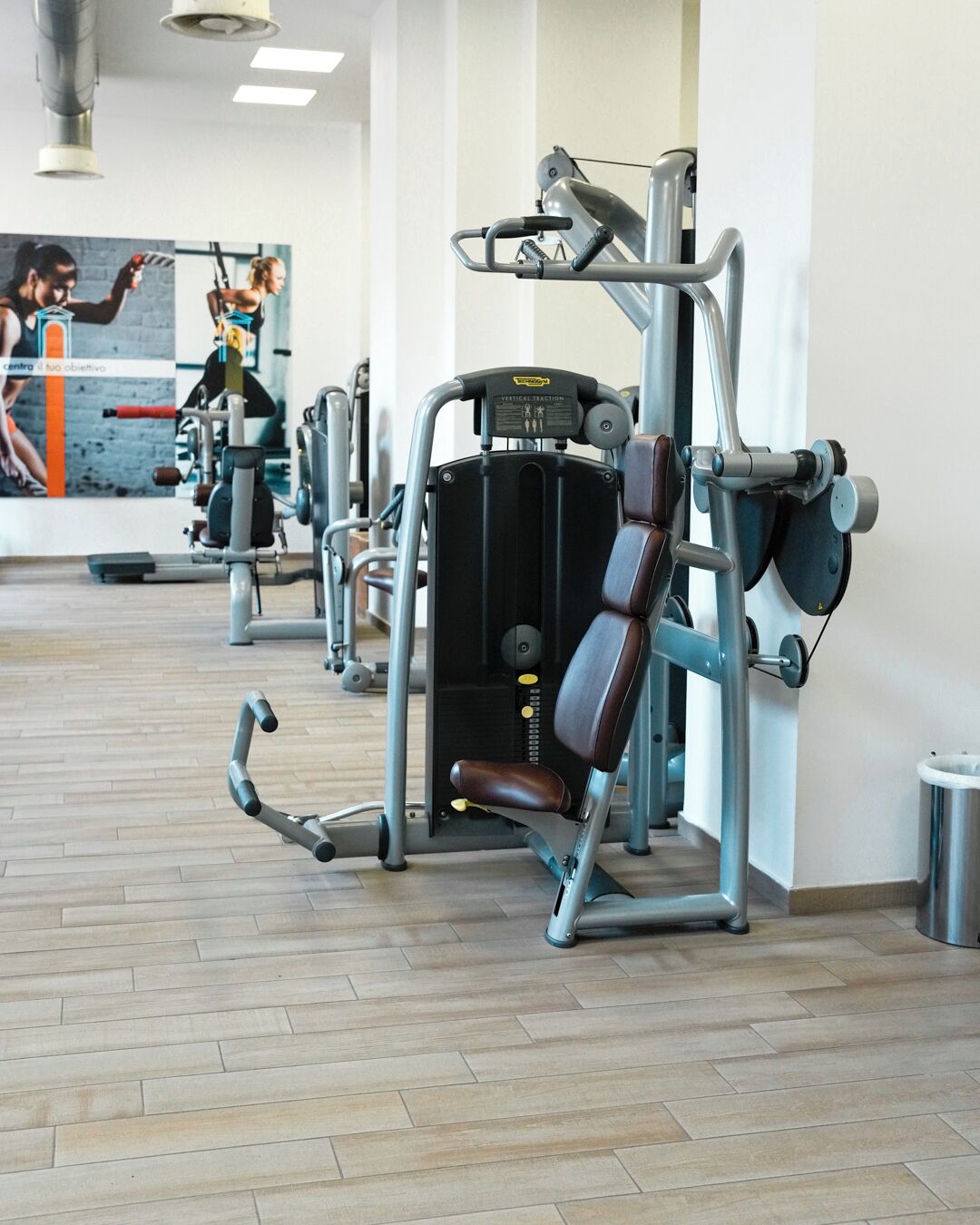 Una palestra con macchinari da allenamento, uno specchio e un pavimento in legno.