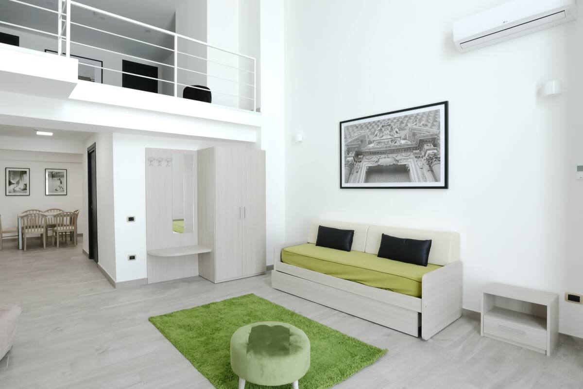 Un espacio habitable moderno y de planta abierta, con techos altos, una zona de comedor y una escalera que conduce a un nivel superior.