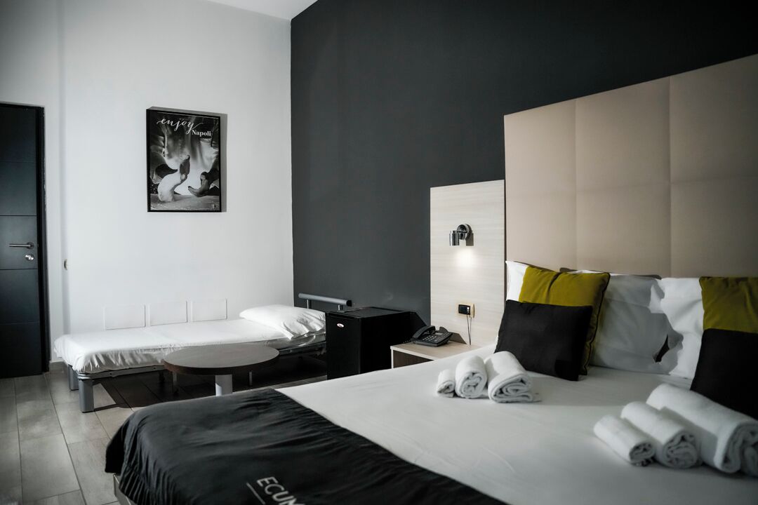 Una habitación de hotel moderna con una cama grande, una cama individual, un escritorio y una silla. Hay un cartel en la pared y una ventana con persianas.