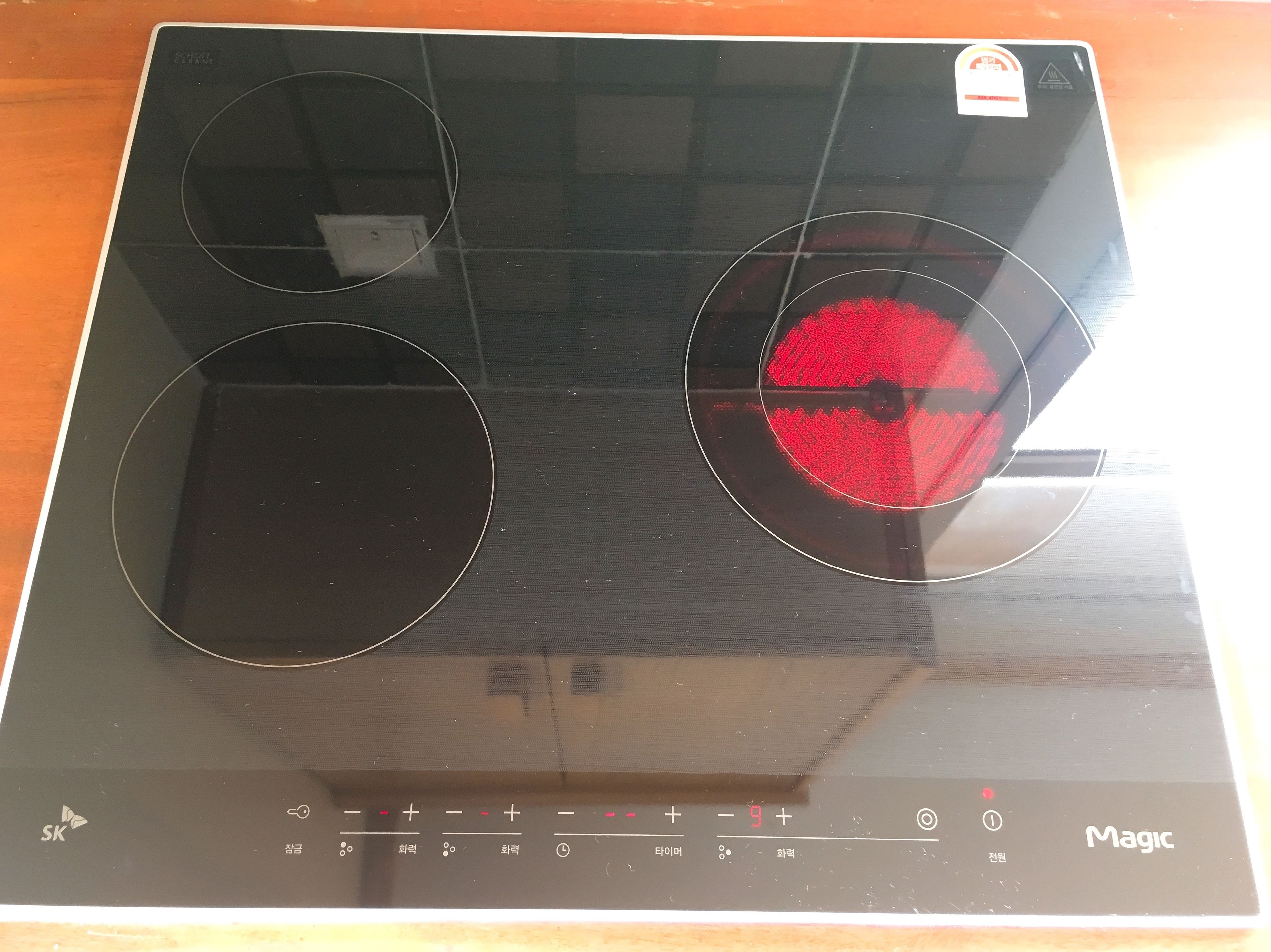 Una cocina de inducción negra con panel de control digital y luz indicadora roja.