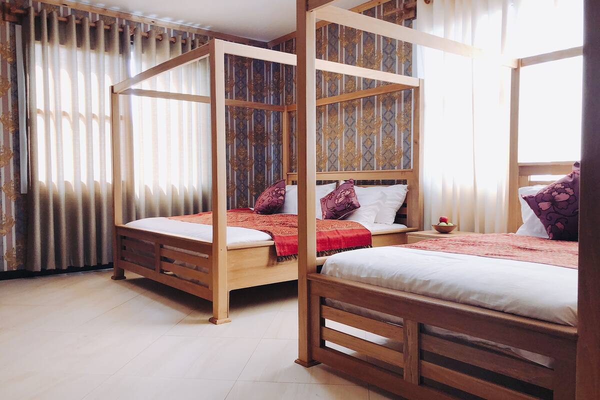 A room with two wooden beds, each with a canopy, and a large window with curtains.