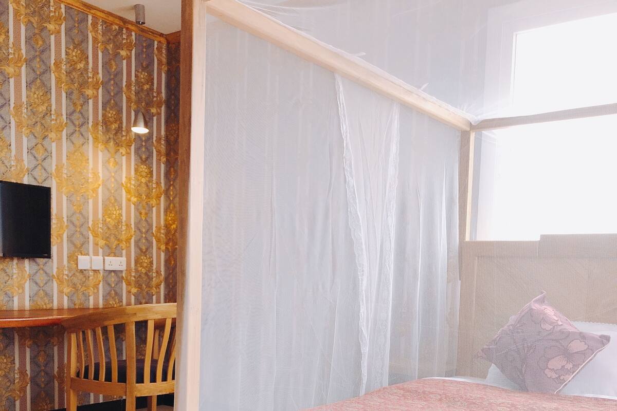 A bedroom with a four-poster bed, a desk with a chair, and a television on the wall.