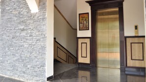 Un ascensor moderno con paneles de madera, una escalera con barandillas de madera y una pared de piedra.
