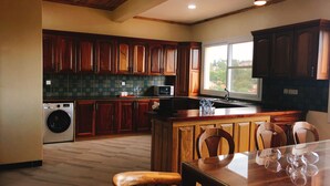 Una cocina con armarios de madera, lavadora integrada, mesa de comedor con cubierta de vidrio y vistas al exterior.