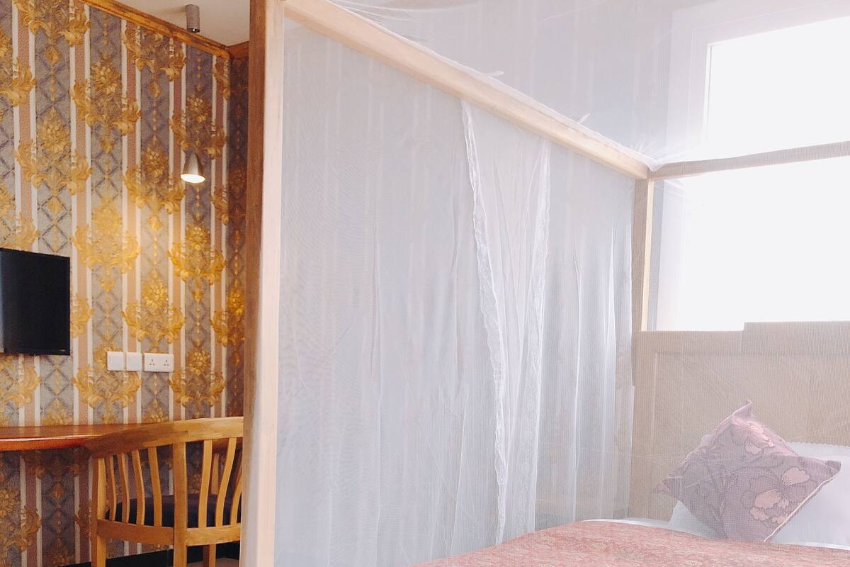 A bedroom with a four-poster bed, a desk with a chair, a television, and a window.