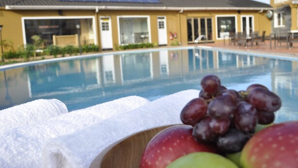 Una piscina con vista despejada a un edificio al fondo, un cuenco de fruta y una toalla blanca.