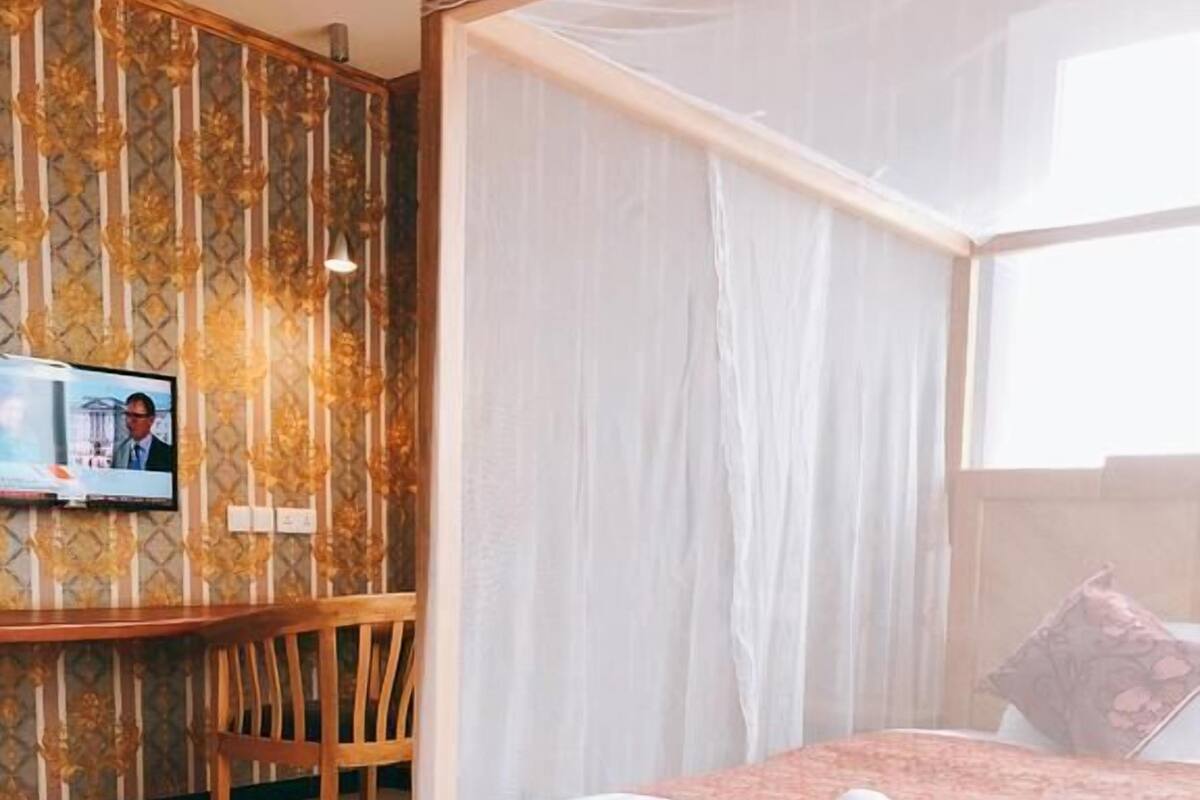 A bedroom with a four-poster bed, a wooden desk, and a television on the wall.