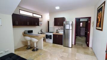 Compact kitchen with microwave, gas stove, and refrigerator, featuring a breakfast bar with two stools.