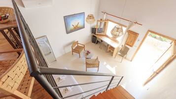 A spacious room with a wooden staircase, a dining area with a table and chairs, and a large window providing natural light.