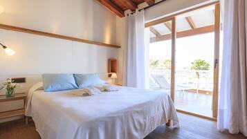 A neatly made bed with pillows, a bedside table with a lamp, and a view of an outdoor balcony.