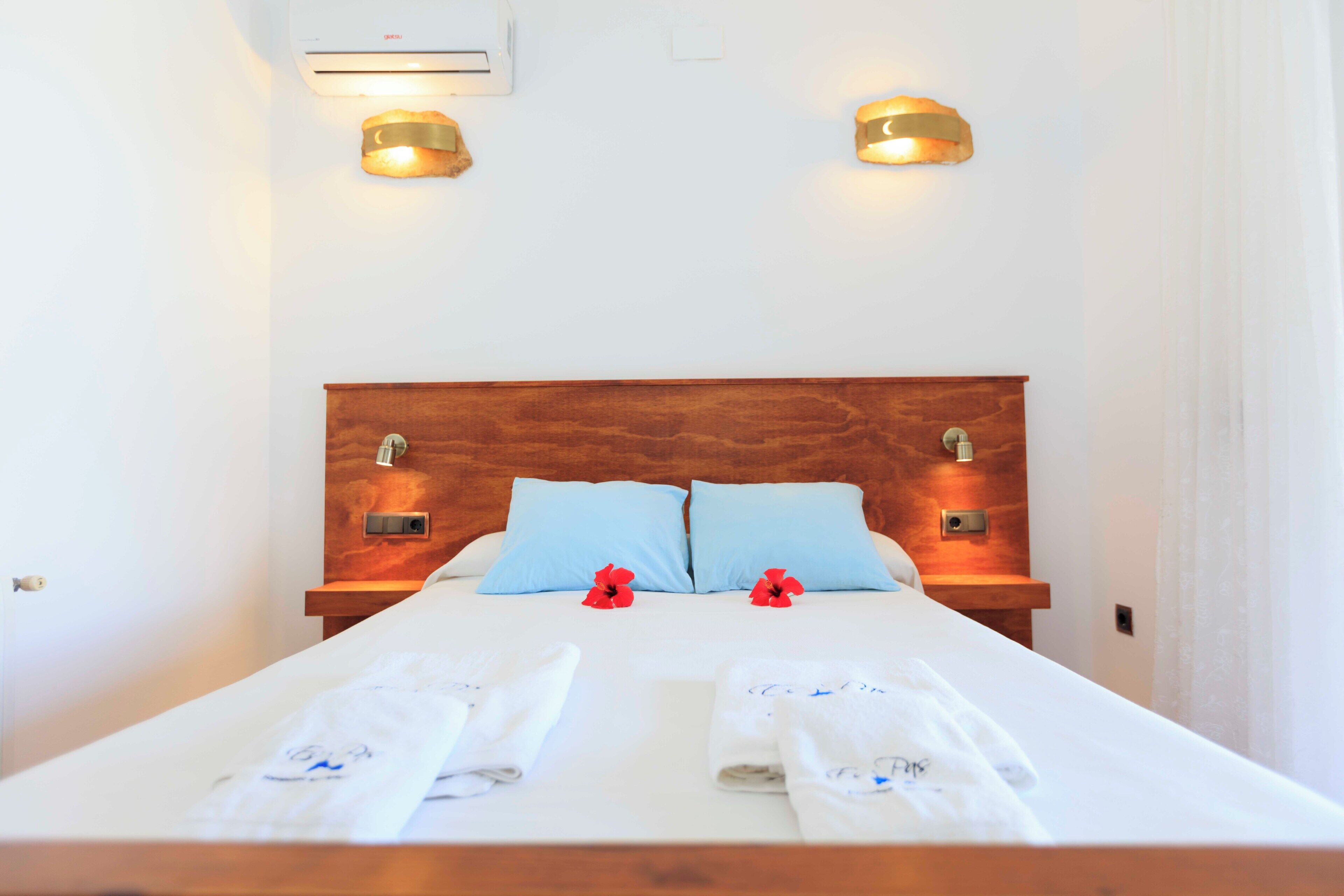 A neatly made bed with two pillows, a wooden headboard, and two wall-mounted lights.