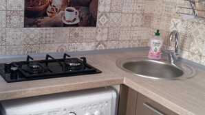 A compact kitchen with a gas stove, a built-in washing machine, a sink, and a tiled backsplash. - Hostel Voyage (Kyiv)