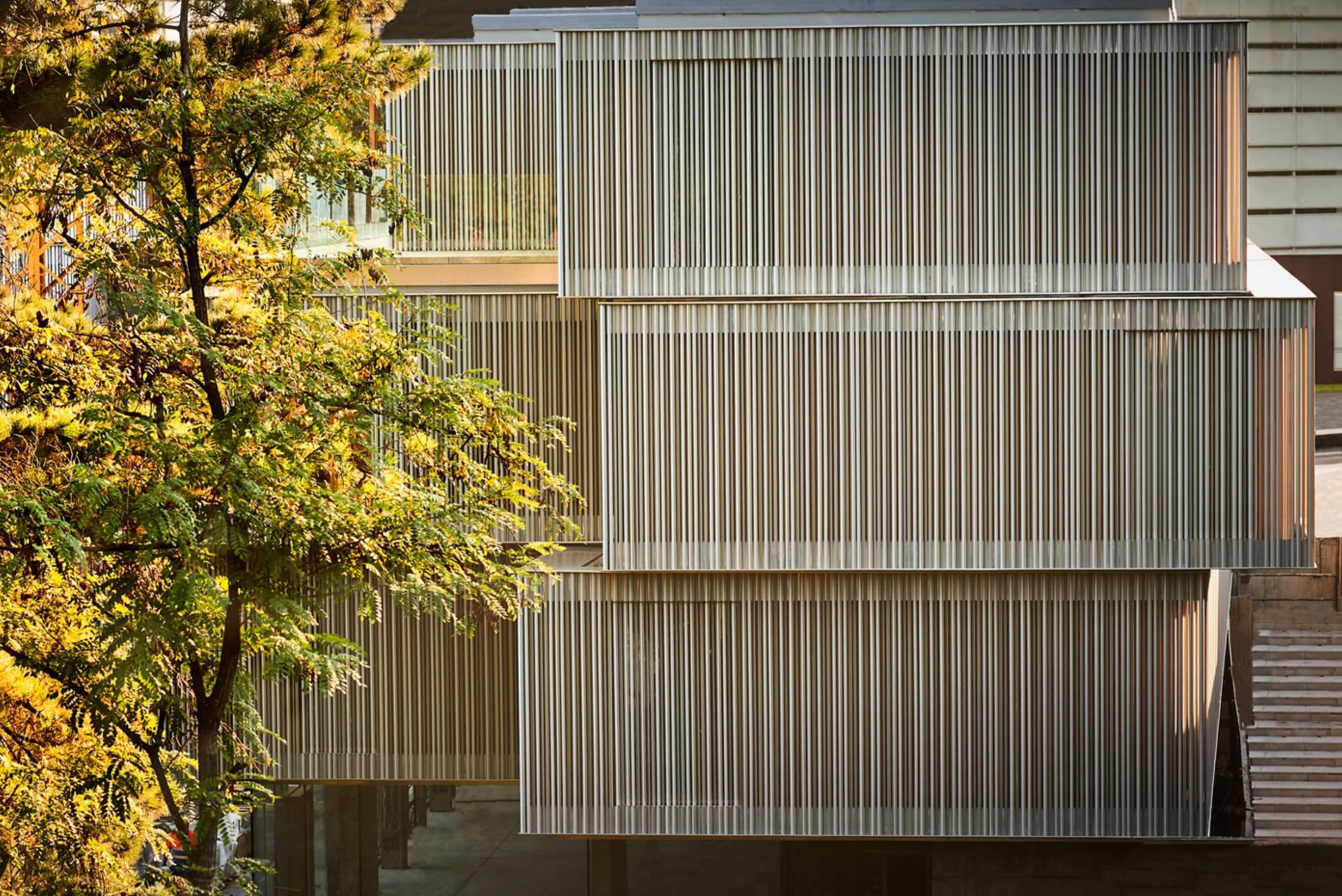 Een modern gebouw met verticale panelen en een boom op de voorgrond.