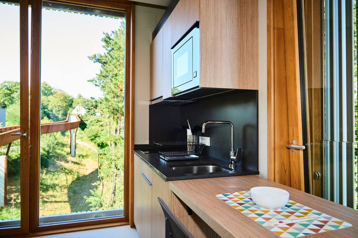 A modern kitchen with a large window, wooden cabinets, a black countertop, and a sink.