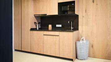 Une cuisine compacte avec des meubles en bois, un plan de travail noir, un four à micro-ondes, un évier et une poubelle à rayures.