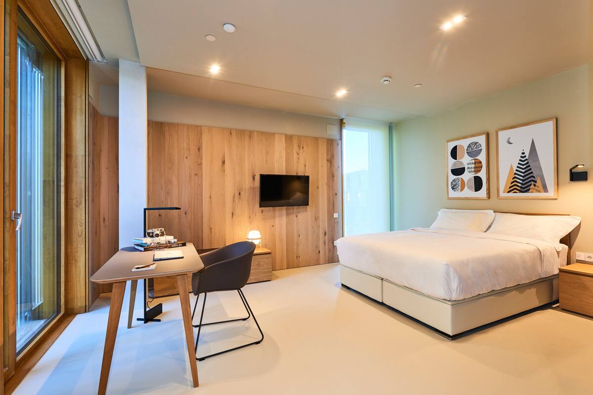 A modern bedroom with a bed, a desk, a chair, a TV, and artwork on the wall.