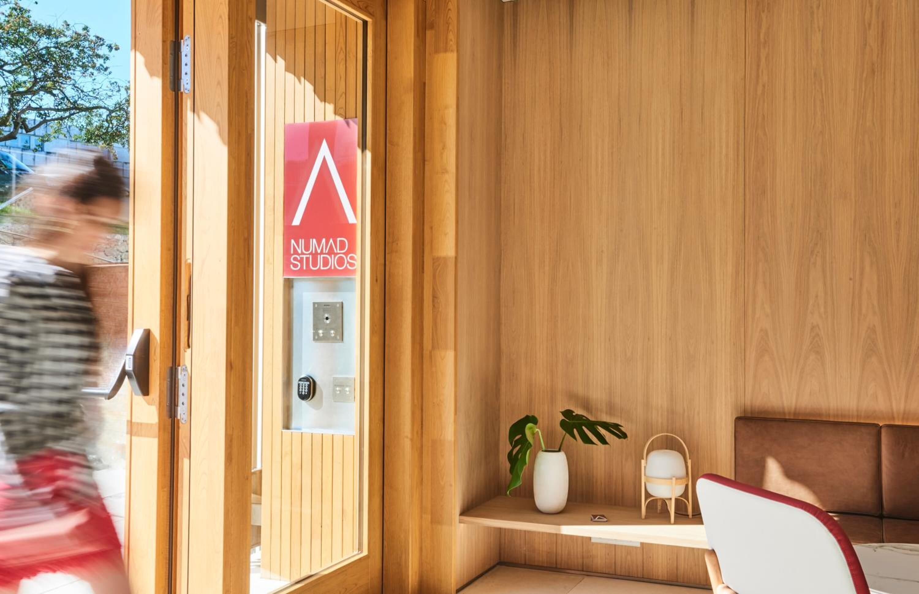 Un intérieur moderne avec un mur lambrissé en bois, un comptoir d’accueil, un espace détente et une enseigne indiquant « NUMAD STUDIOS ».