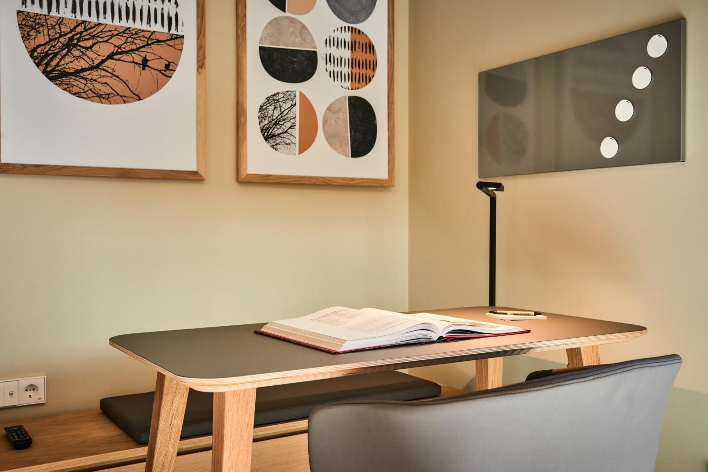 Una habitación moderna con un escritorio de madera, una silla, una lámpara y cuadros en la pared.