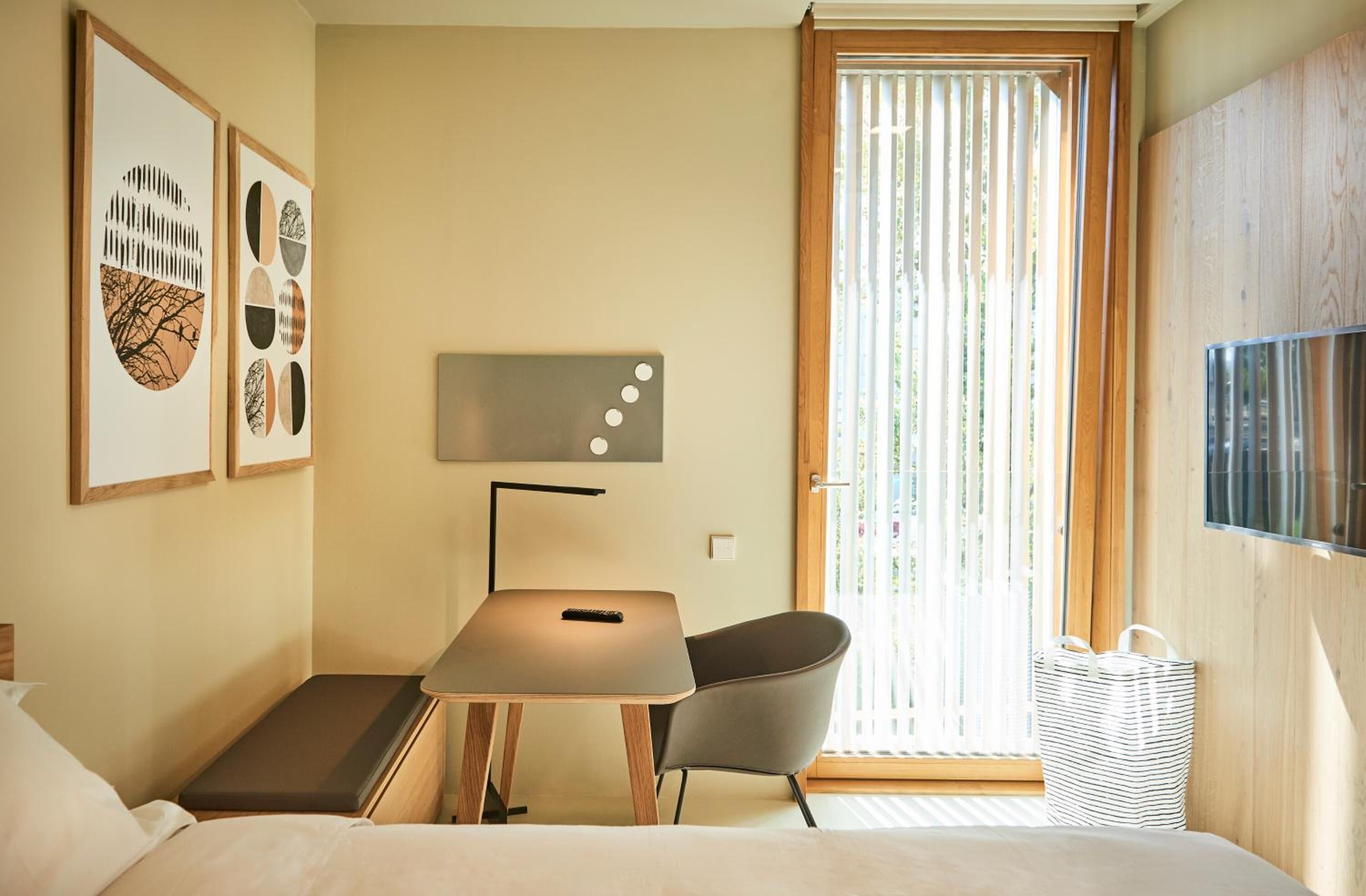 Una habitación de hotel con una cama, un escritorio con silla, un televisor y obras de arte en la pared.