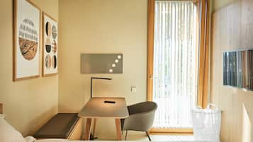 Una habitación de hotel con una cama, un escritorio con silla, un televisor y obras de arte en la pared.