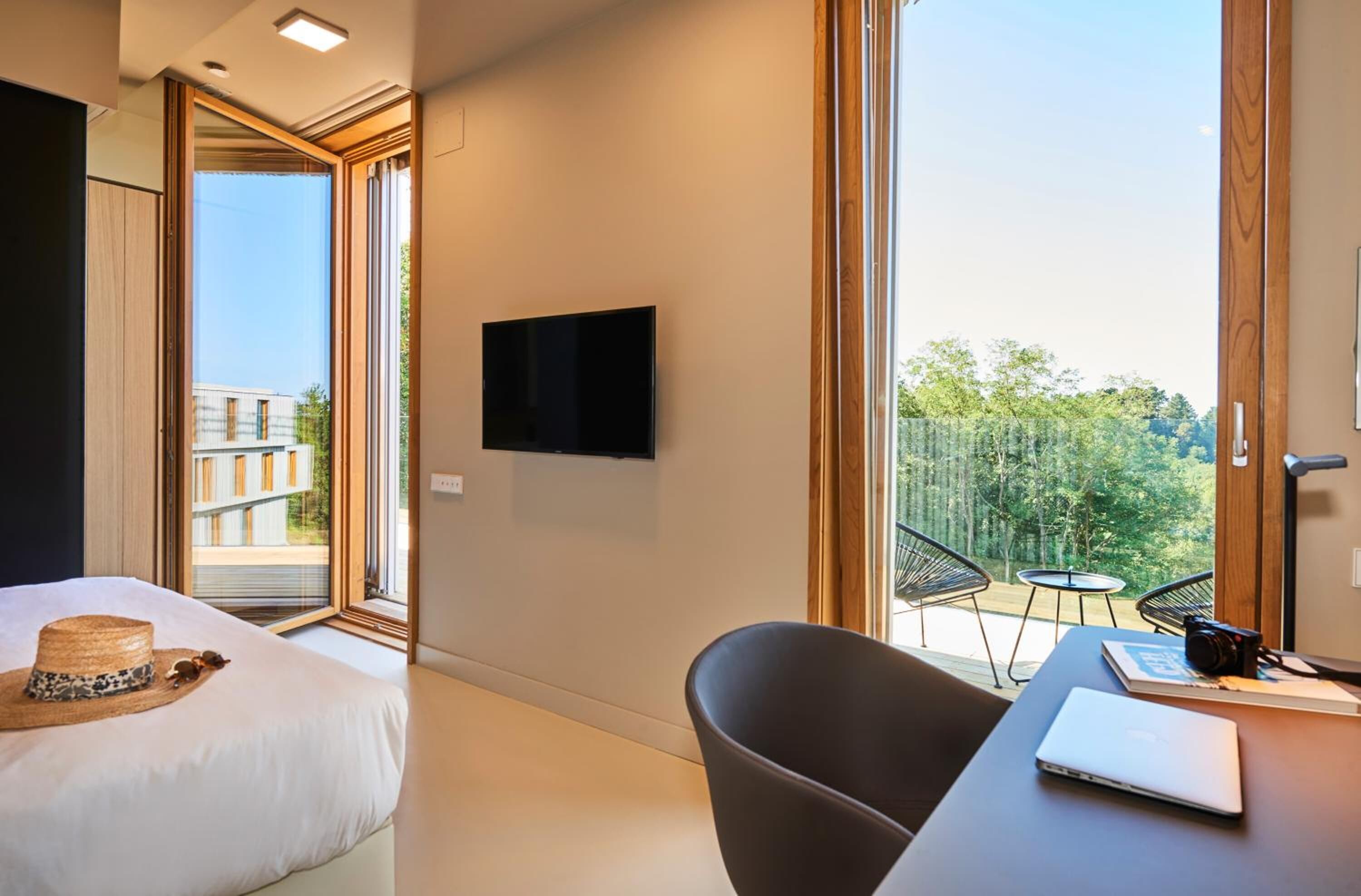 Habitación de hotel con cama, escritorio con computadora portátil, televisor y balcón con sillas.