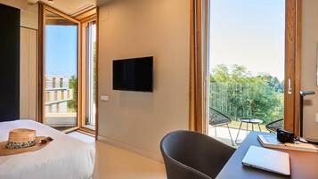 Habitación de hotel con cama, escritorio con computadora portátil, televisor y balcón con sillas.