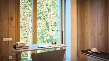 A wooden room with a desk, chair, and a view of trees through large windows.