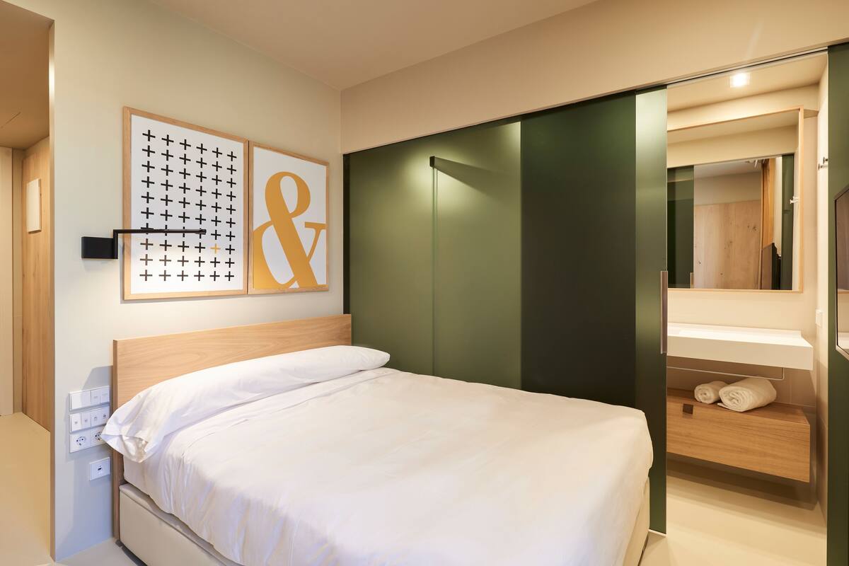 A modern hotel room with a large bed, a wardrobe, and a mirror.