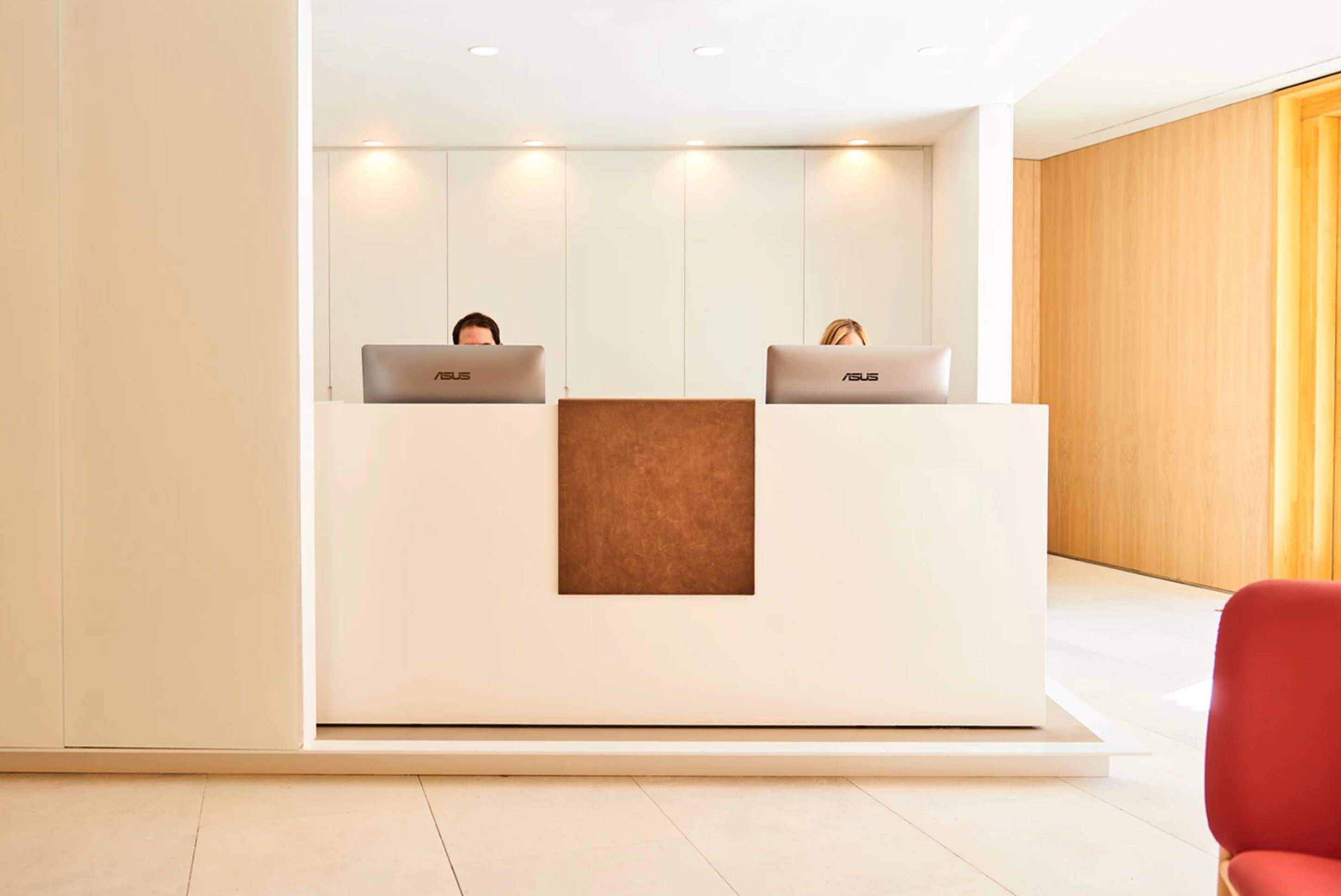 A reception desk with two laptops, a brown accent wall, and a red chair.