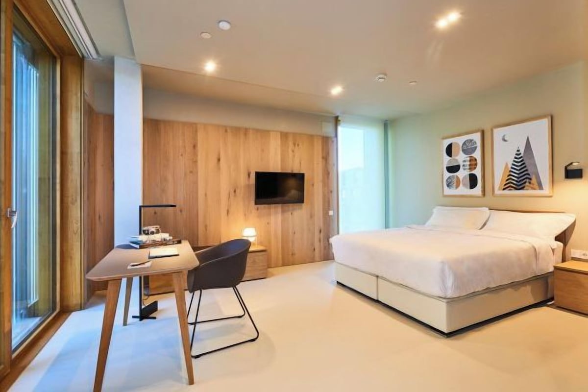 A modern bedroom with a bed, desk, chair, and a TV mounted on the wall.