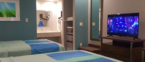 Une chambre d’hôtel avec deux lits, une télévision, une salle de bain et un miroir.