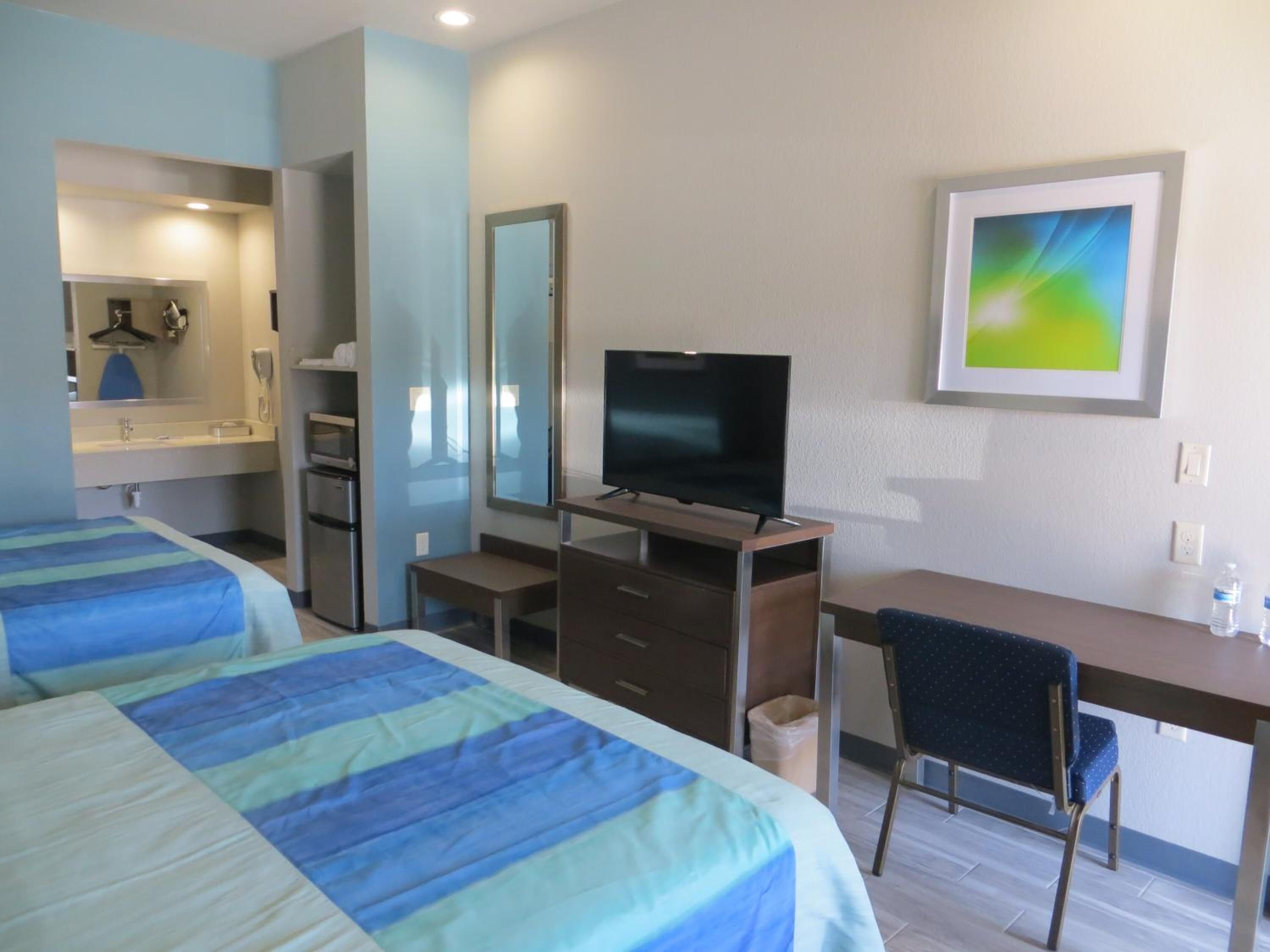Une chambre d’hôtel avec deux lits, un bureau, une télévision, une chaise et une salle de bain équipée d’un miroir et d’un lavabo.