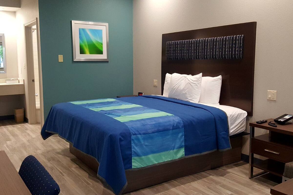 Une chambre d’hôtel équipée d’un lit, d’un bureau, d’une chaise, d’une table de chevet et d’un téléviseur fixé au mur.
