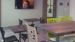 Een vergaderzaal met een grote tafel, meerdere stoelen, een aan de muur bevestigde televisie en een plafond met blauwe verlichting.