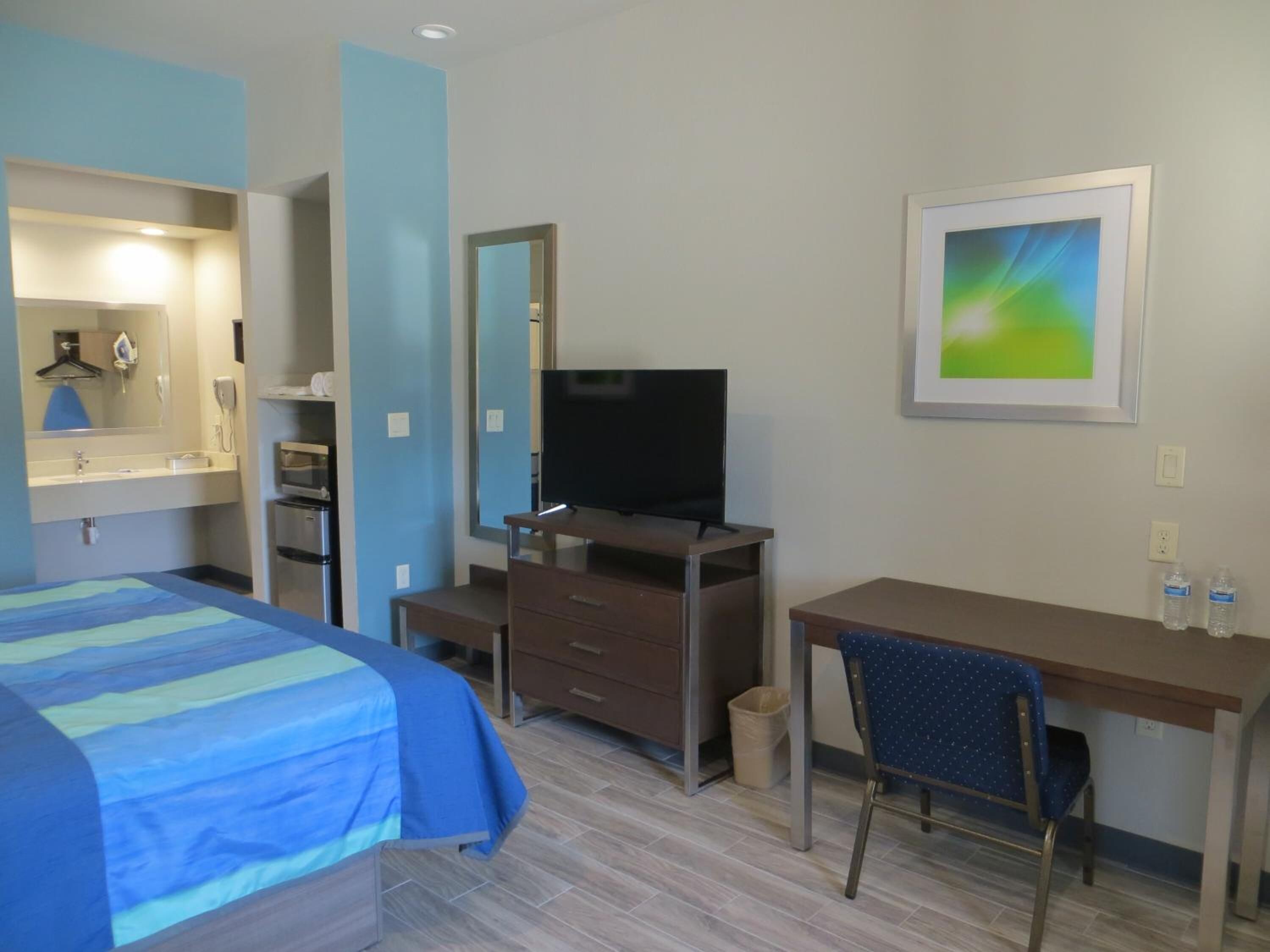 A hotel room with a bed, a desk, a chair, a television, a mirror, and a framed picture on the wall.