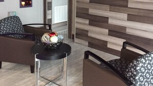 Een moderne hotelkamer met een houten wandpaneel, een flatscreen televisie aan de muur, een ronde tafel met decoratieve kom en twee gestreepe fauteuils.