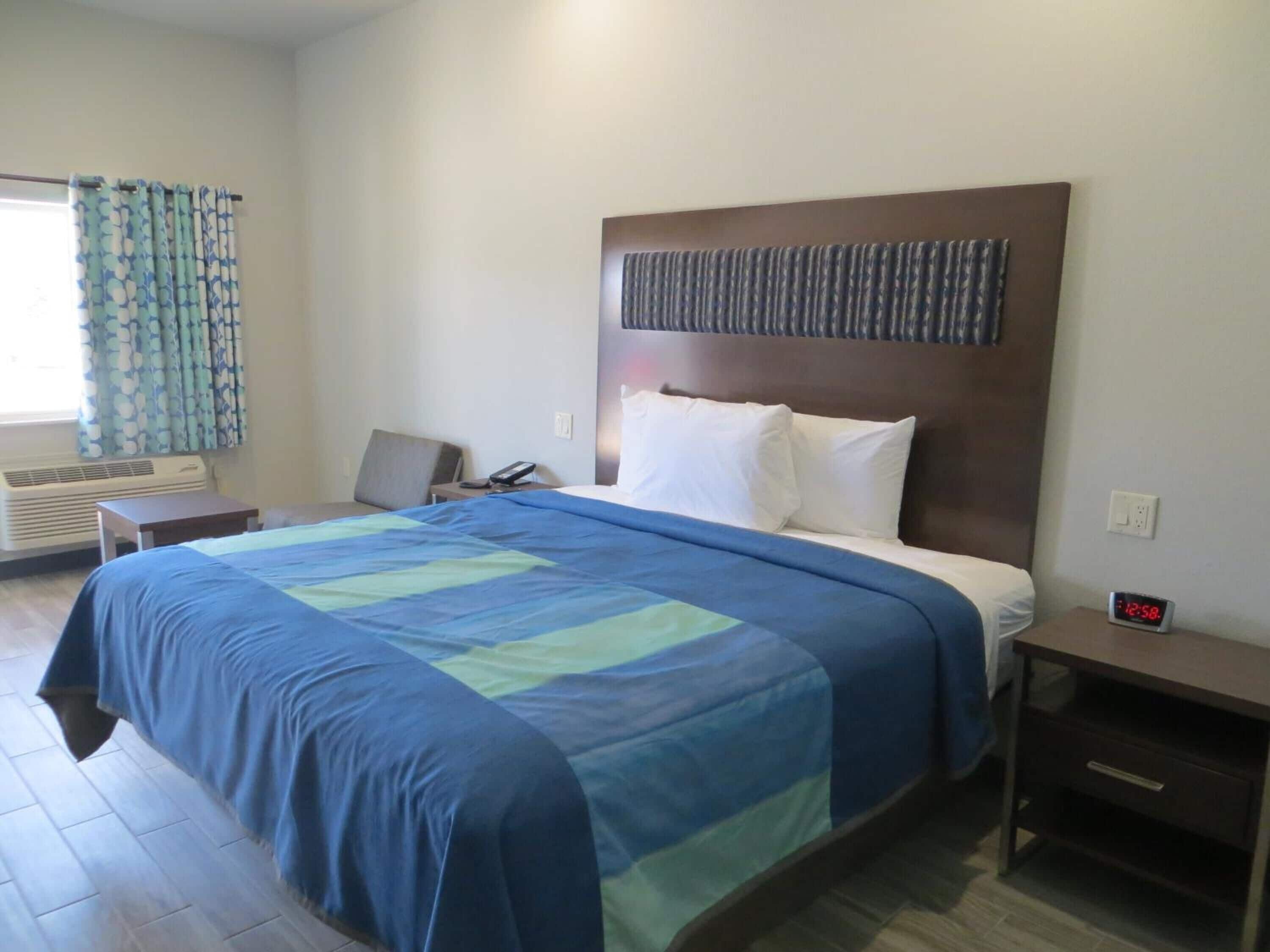 A hotel room with a bed, bedside table, alarm clock, and a window with curtains.