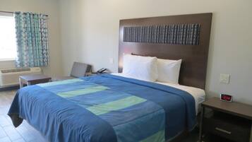 Une chambre d’hôtel avec un lit, une table de chevet, un réveil et une fenêtre avec des rideaux.