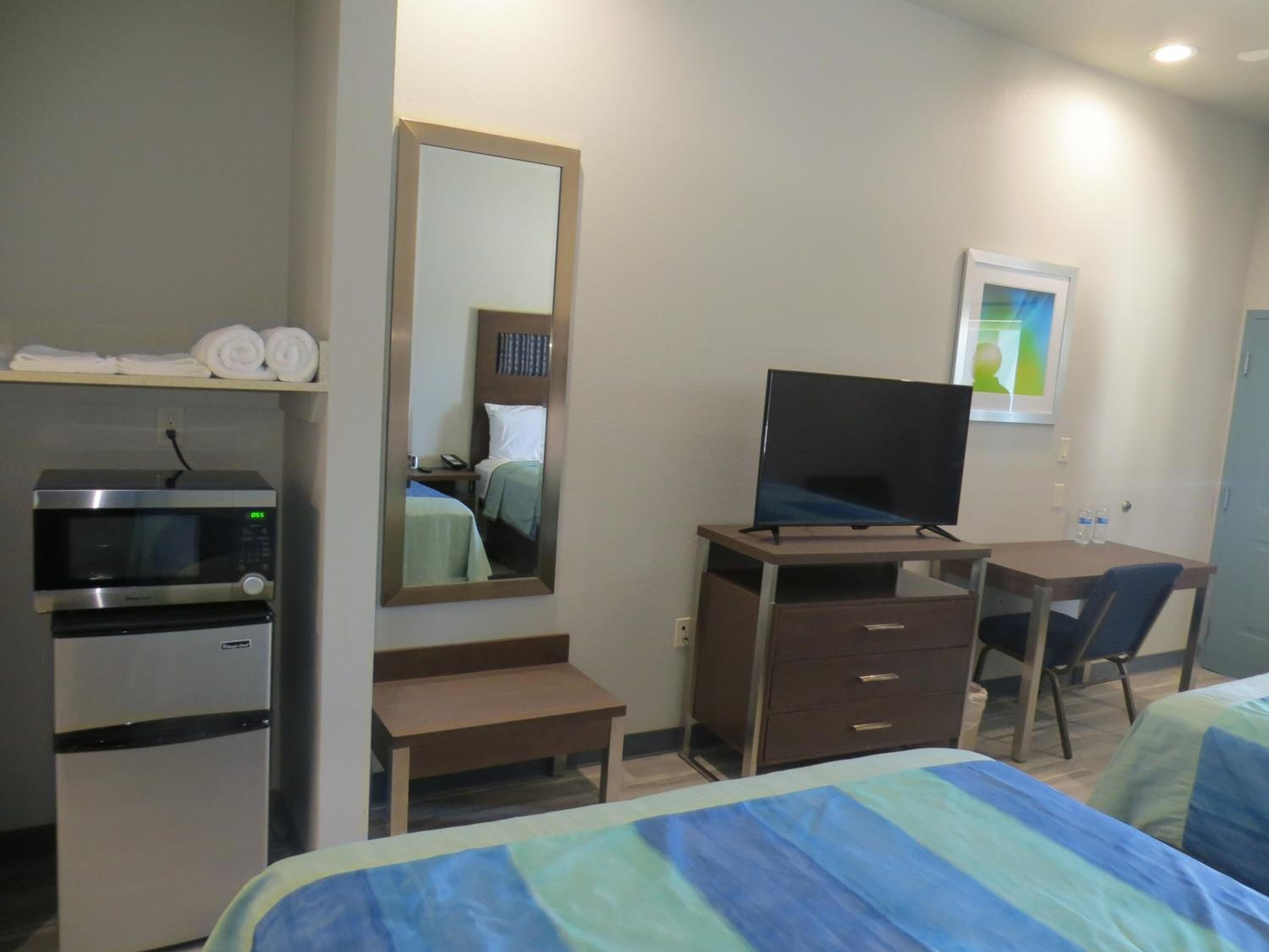 A hotel room with a bed, a desk with a television, a microwave, a refrigerator, and a mirror.