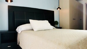 A neatly made bed with a white comforter and pillows, flanked by black nightstands with drawers, under two hanging pendant lights.