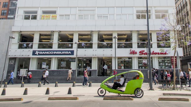 A multi-story building with a modern architectural design, featuring a large number of windows and a ground-level commercial space with visible signage for a bank and a store.