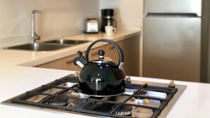 A kitchen with a gas stove, a kettle, a coffee maker, and a refrigerator.