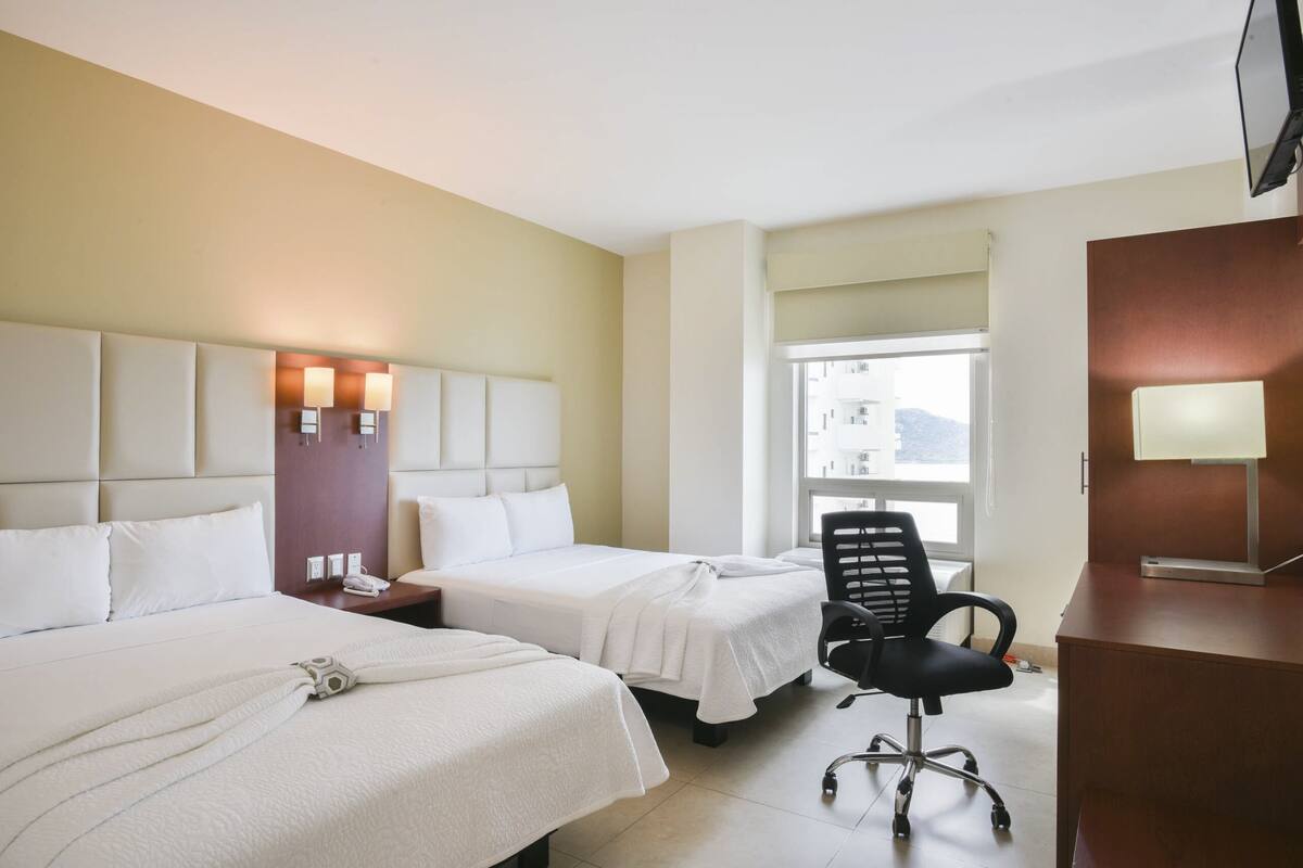 A hotel room with two beds, a desk, a chair, and a TV.