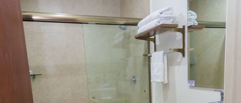 A bathroom with a glass-enclosed shower, a white toilet, a sink, and a trash bin.