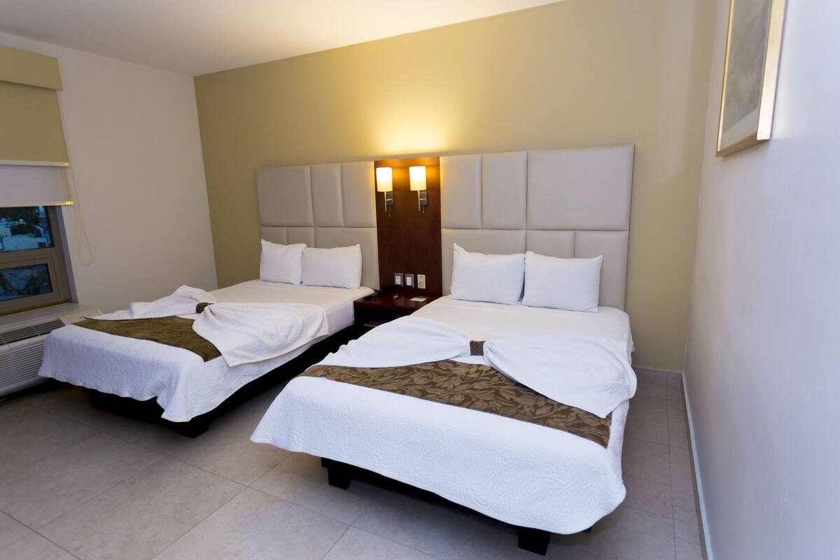 A hotel room with two beds, a large headboard, and a wall-mounted TV.