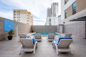 Zona de piscina al aire libre con sillas de descanso y un cartel.