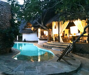 A swimming pool with stone tiles, a thatched-roof structure, and a seating area with a lamp. - Simba Wa Kale (Malindi)