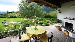 Une terrasse avec une table ronde, des chaises, une cheminée et une vue sur le jardin.
